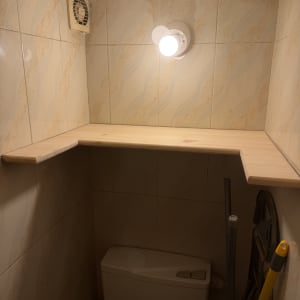 מדף עץ מעל אסלה עם מנורה ומאוורר קיר