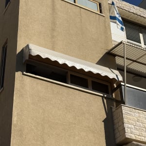 סוכך חלון מתקפל עם בד לבן מותקן על חזית בניין