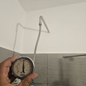 מד לחץ מים מוחזק ביד ליד צינור במקלחת