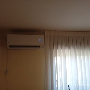 מזגן מותקן על קיר ליד חלון עם וילון לבן