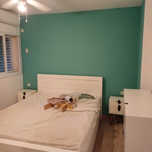 חדר שינה עם מיטה לבנה, קיר ירוק וכלי עבודה על המיטה