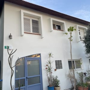 אדם עובד בגינה ליד בית עם חלונות תריסים