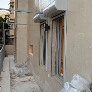 חלונות אלומיניום עם תריסים חיצוניים מותקנים על קיר בניין.