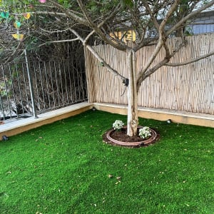 עץ בגינה עם דשא מלאכותי ופרחים לבנים