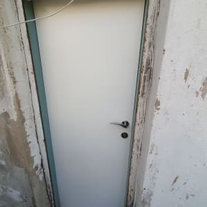 דלת לבנה עם ידית מתכת במסגרת קיר מתקלף