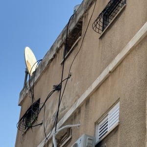 צלחת לוויין, מזגן וחוטי חשמל על קיר בניין