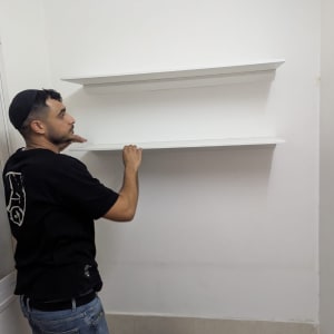 אדם מתקין מדפים לבנים על קיר לבן