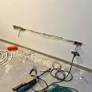 קיר עם חוטי חשמל, כלי עבודה וכבלים על הרצפה