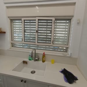 תריסים מותקנים מעל כיור במטבח עם ברז וחומרי ניקוי