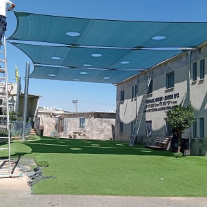 התקנת סוכך בחצר עם דשא סינתטי ואדם על סולם