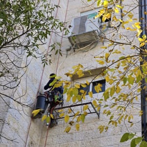 אדם עובד בגובה על פיגום ליד קיר בניין