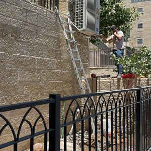 אדם עובד על מזגן על קיר חיצוני עם סולם