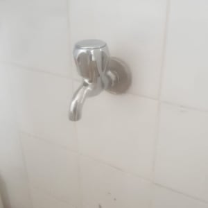 ברז מתכת מותקן על קיר אריחים לבנים