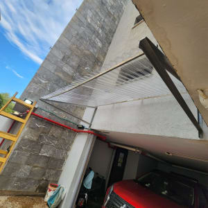 חניה עם רכב אדום ומבנה עם גגון מתכת