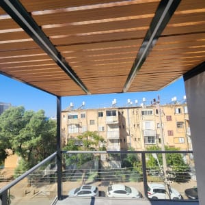 פרגולה מאלומיניום במרפסת עם נוף לבניינים ועצים