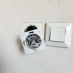 שקע חשמלי פתוח עם חוטים חשופים ליד מתג קיר