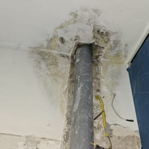 צינור שחור בקיר עם סימני רטיבות ועובש