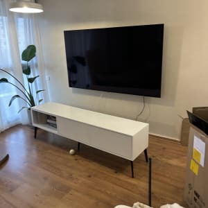 טלוויזיה מותקנת על קיר עם שידה לבנה מתחת