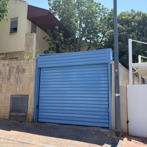 שער חשמלי כחול ליד בית ועץ