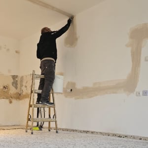 אדם על סולם מבצע תיקוני קיר בחדר