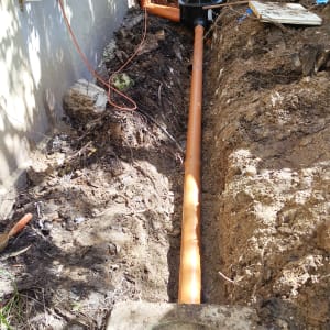 צינור כתום מונח בתעלה ליד קיר בניין