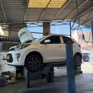 רכב קיה לבן מורם על ליפט במוסך עם מכסה מנוע פתוח