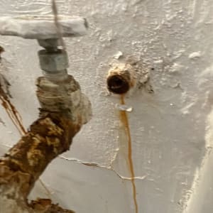 צינור חלוד עם נזילה על קיר לבן