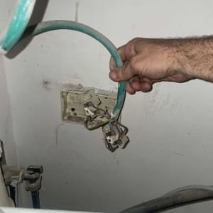 יד מחזיקה חוט חשמל ליד שקע פתוח בקיר