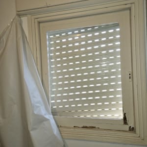 תריסים לבנים על חלון עם וילון לבן בצד