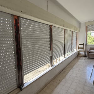 מערכת תריסי גלילה לבנים במרפסת סגורה במהלך עבודות התקנה או תיקון