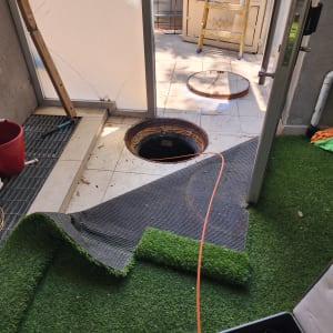 פתח ביוב פתוח עם כבל כתום על דשא סינתטי