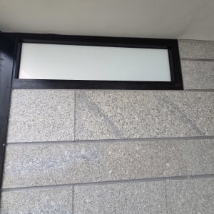 חלון אלומיניום שחור צר עם זכוכית חלבית בקיר מחופה אבן