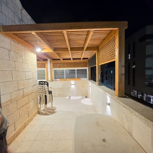 פרגולת עץ מוארת במרפסת דירה עם הצללת שלבים ושבכיות עץ