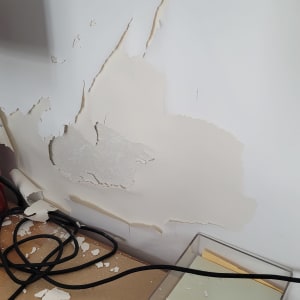 קיר עם צבע מתקלף וחתיכות צבע על הרצפה