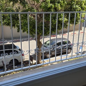 מעקה מתכת לבן עם עיטורים מול חלון פתוח לרחוב