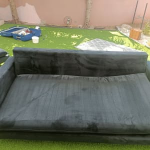 ספה שחורה על דשא עם כלי ניקוי ברקע