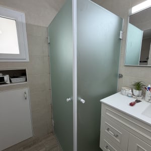 מקלחון זכוכית בחדר אמבטיה עם כיור ומראה