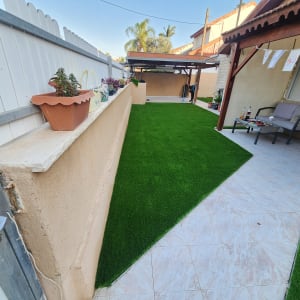 דשא סינתטי עם עציצים על קיר בגינה פרטית