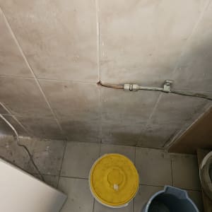 צינור דולף בקיר עם דלי ומגב על הרצפה