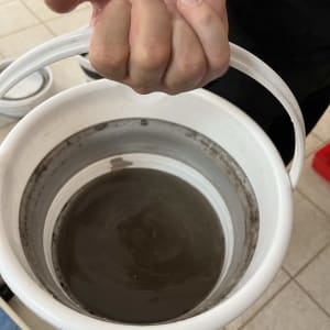 יד מחזיקה דלי עם מים מלוכלכים, כנראה קשור לניקוי מזגן