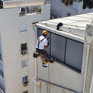 אדם עם קסדה צהובה עובד בגובה על בניין