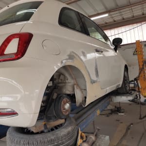 רכב לבן בתיקון פחחות במוסך, ללא גלגל אחורי