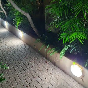 תאורה עגולה מותקנת על קיר נמוך ליד שביל