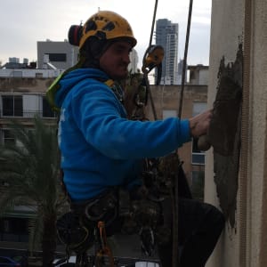 אדם עם קסדה מורח חומר איטום על קיר חיצוני