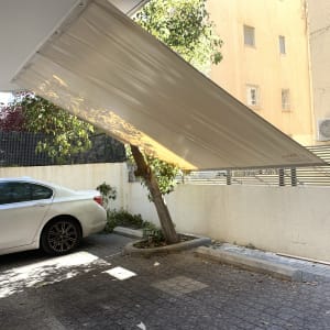 סוכך לבן תלוי מעל חניה עם עץ תומך