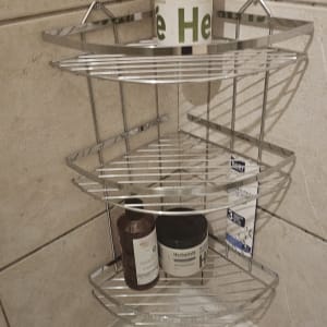 מדף מתכת בפינת מקלחת עם בקבוקי שמפו וסבון