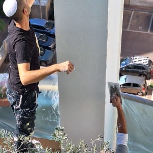 שני אנשים צובעים קיר חיצוני עם שפכטלים