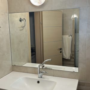 התקנת מראה מלבנית גדולה על קיר אריחים מעל כיור בחדר רחצה