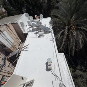 גג אטום עם צלחות לוויין ועצים ברקע