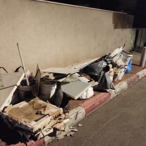 ערימת פסולת בנייה על מדרכה ליד קיר חיצוני.